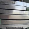 Cạnh các cuộn đai thép mạ kẽm xếp chồng, có miếng nhựa xanh kẹp giữa các cuộn