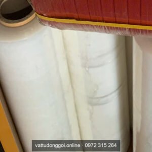 Cuộn màng PE quấn pallet màu trắng đặt trên kệ, bên dưới cuộn dây đai đỏ